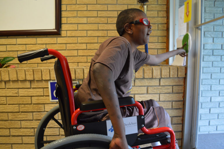 A boy who uses a wheelchair looks outside a door as he opens it.