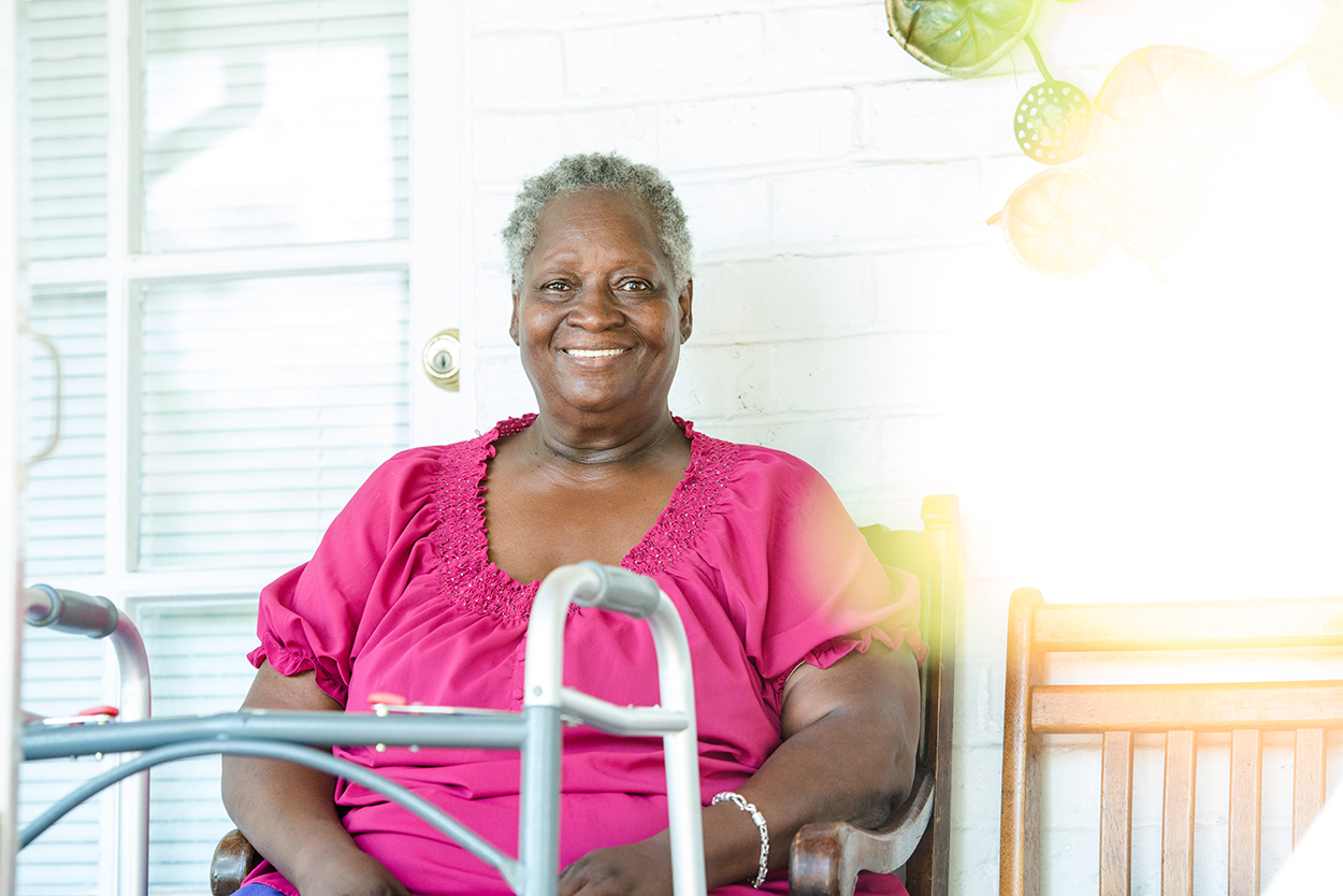 A woman in a pink shirt smiles. A walker is in the foreground.