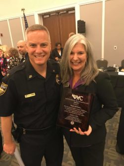 Angie McKinley holding an award next to a police officer